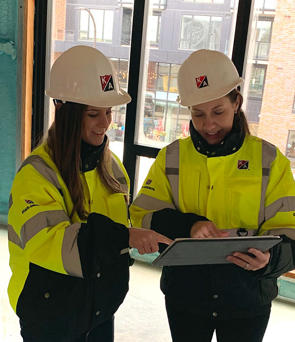 Two employees in safety jackets review a tablet computer