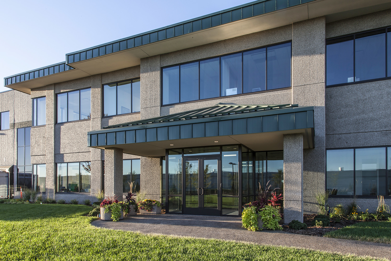 "Uline was begun in 1980 in the basement of the owners’ home. The first product offered was the H-101 carton sizer, which is still offered today. Uline has grown steadily since 1980 and continues to be a family owned and operated business. Today, with over 2,500 employees nationwide, Uline has distribution centers near Chicago, IL; Minneapolis, MN; Allentown, PA; Los Angeles, CA; Atlanta, GA; Dallas, TX; Seattle, WA; Tijuana, Mexico; Monterrey, Mexico and near Toronto, Ontario. The new Uline Distribution Warehouse, constructed by Kraus-Anderson, is located in Hudson, WI at Highway 35 and Hanley Road. The project was constructed on a 62.5 acre site. The 646,000 s.f. facility consists of 610,000 s.f. of warehousing with a 32’ clear height at the first column line and 36,000 s.f. of office space. The site development, including underground utilities, storm water ponds, erosion control, grading and landscaping was included in the scope of work. Exterior pavements include a concrete truck court area and bituminous parking areas. This building is a cross-dock warehouse with approximately 182 dock positions with parking for 200 additional trailers. Primary construction is IBC Type 2B, non-combustible, fully sprinklered, utilizing pre-cast concrete wall panels with steel structure and ballasted EPDM roofing over metal deck. Uline stores contents that are classified as Commodities I-IV per the NFPA 1 Fire Code, necessitating ESFR sprinkler coverage in the warehouse. The office space is two stories in height, with a pre-cast concrete plank 2nd floor supported on a structural steel frame, plus structural steel roof framing. One hydraulic elevator provides accessibility to 2nd floor with parking for 250 employees."